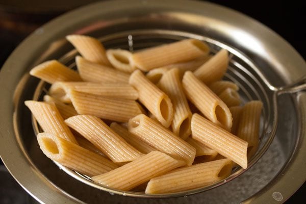 straining the cooked penne pasta. 