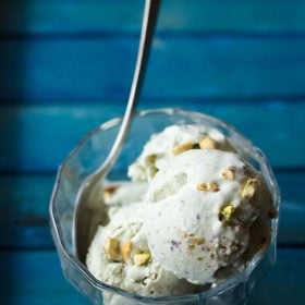 pistachio ice cream scoops in bowl with a spoon on blue table.