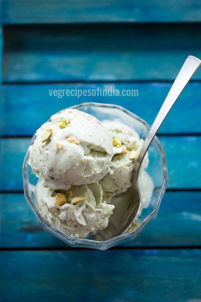 pistachio ice cream scoops in bowl with a spoon on blue table