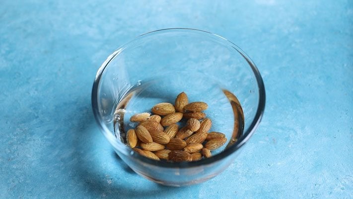 almonds added in a glass bowl placed on a bright light blue board