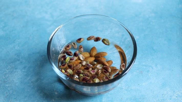pistachios in a glass bowl placed on a bright light blue board