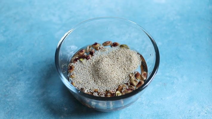 poppy seeds floating on water in a glass bowl placed on a bright light blue board