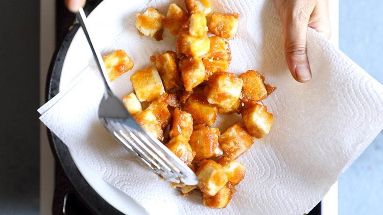 placing fried paneer cubes on a plate lined with paper towels to drain