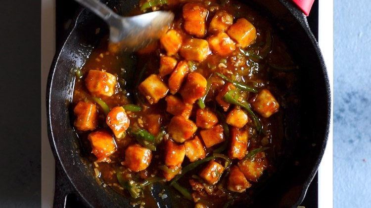 tossing the cubes of paneer in the sauce to coat