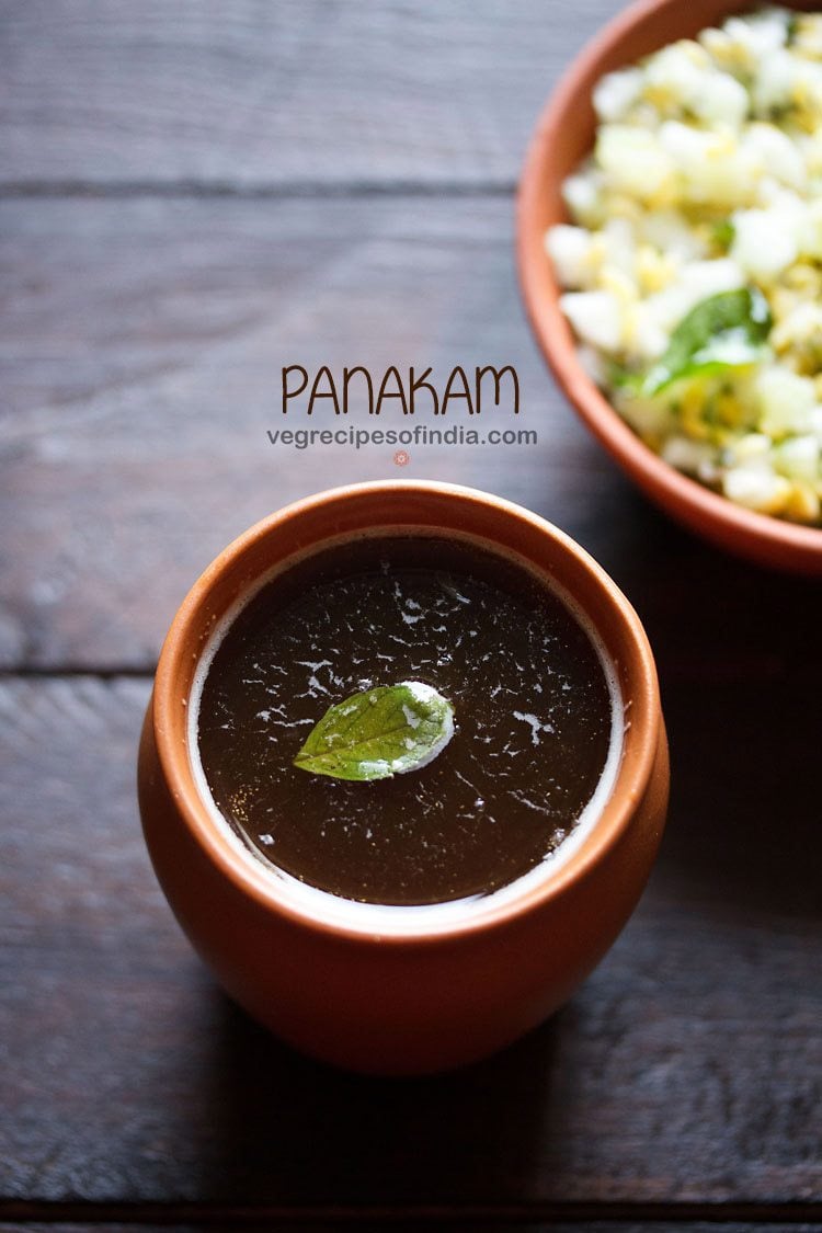 panakam garnished with a tulsi leaf and served in a earthen glass with text layovers. 