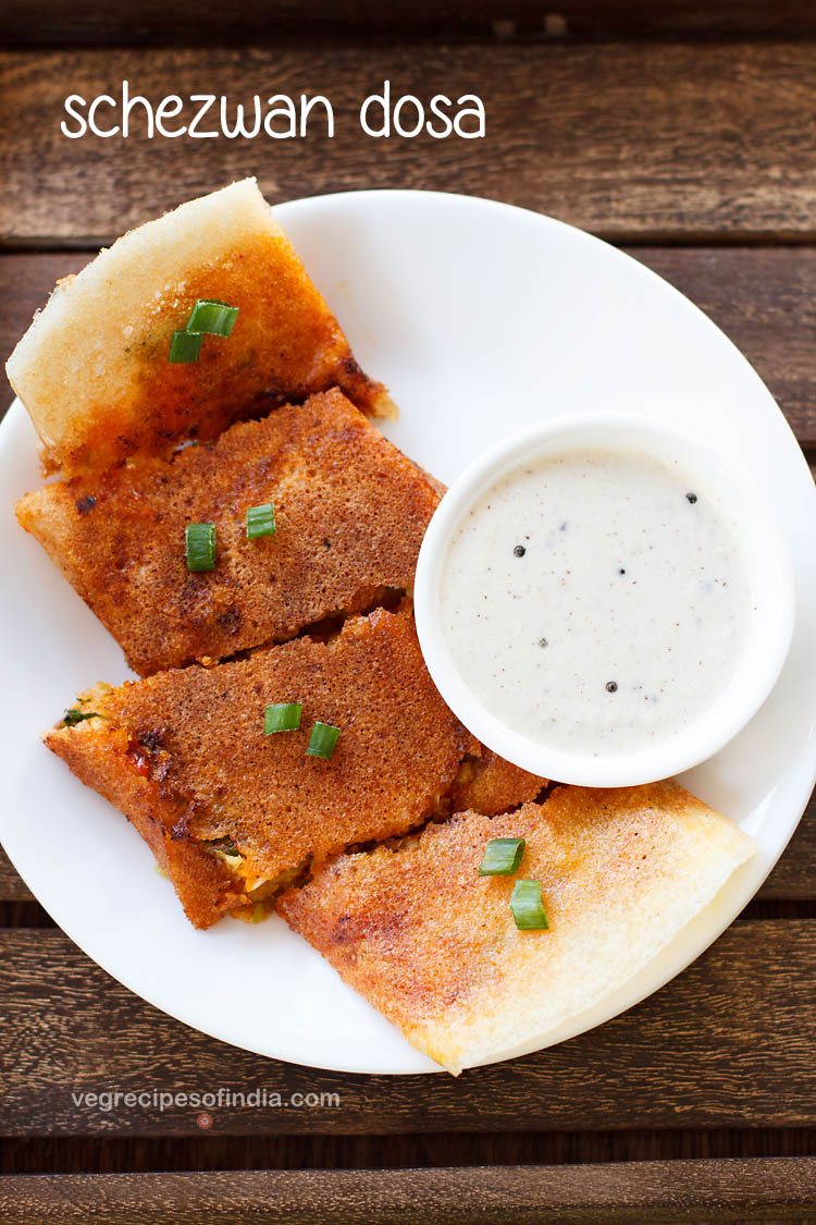 schezwan dosa cut into large pieces and served on a white plate with a bowl of coconut chutney kept on the right side and text layovers. 
