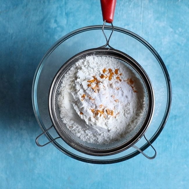 whole wheat flour, all purpose flour, turmeric powder and salt added in a sieve for making dough for holige recipe. 