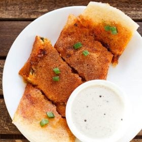 schezwan dosa cut into large pieces and served on a white plate with a bowl of coconut chutney kept on the bottom right side and text layovers.