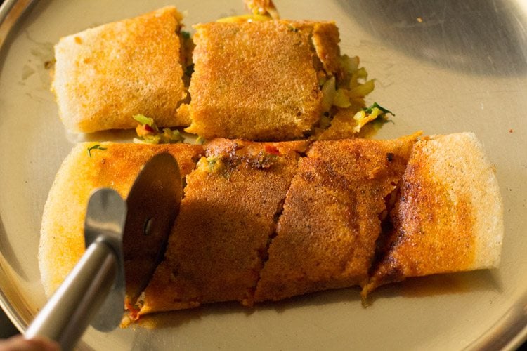 cutting cooked schezwan dosa into parts with a pizza cutter. 