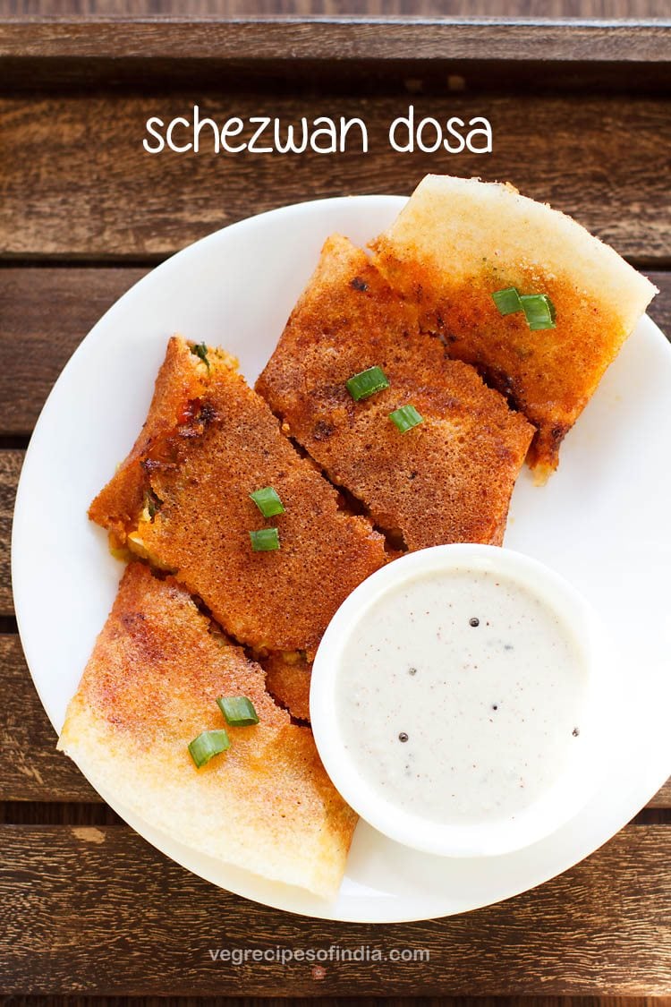 schezwan dosa cut into large pieces and served on a white plate with a bowl of coconut chutney kept on the bottom right side and text layovers.