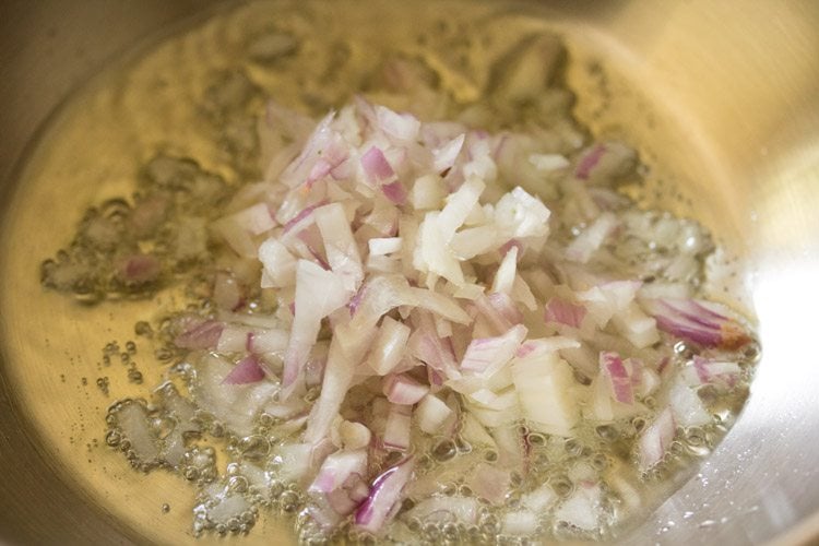 chopped onions added to hot oil in pan for making aloo palak ki sabji. 
