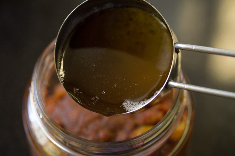 pouring the tempering in the jar containing amla ka achar