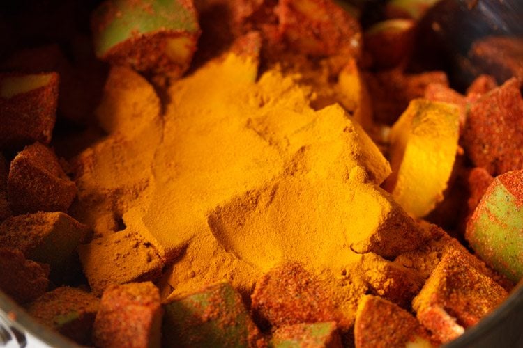 mixing turmeric powder with the spiced mango pieces 
