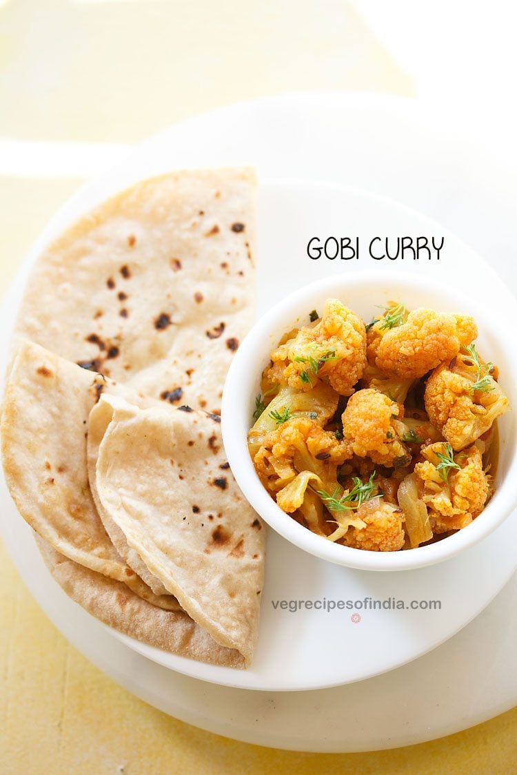 cauliflower curry garnished with coriander leaves and served in a white bowl on a plate of chapattis and text layovers. 