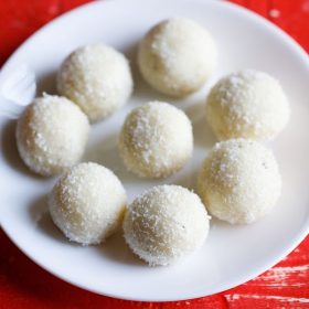 coconut ladoo placed in a circle and in the center on a white plate on a red table