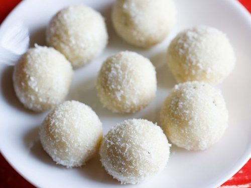 coconut ladoo placed in a circle and in the center on a white plate on a red table