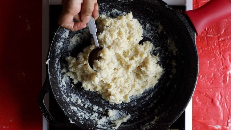 taking a portion of coconut ladoo mixture in measuring spoon