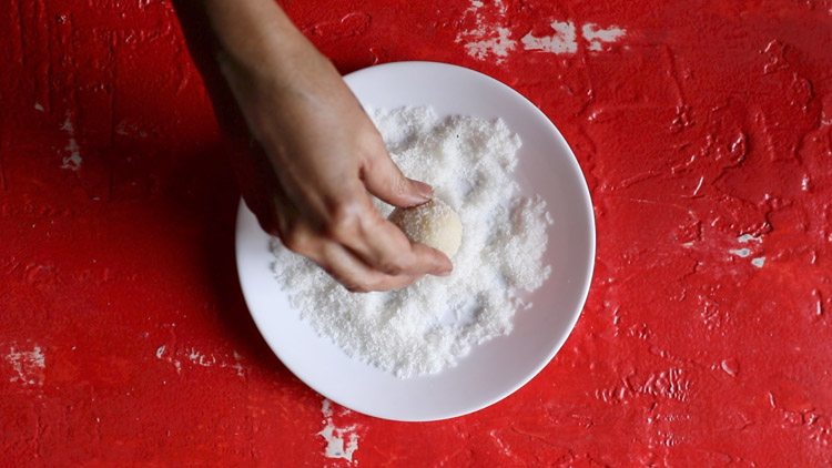 placing coconut laddu on desiccated coconut spread on white plate