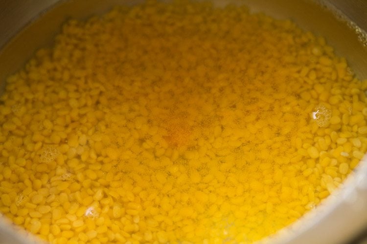moong dal, turmeric powder and water added in a pressure cooker for making moong dal curry. 