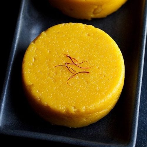 mango kesari garnished with saffron and served on a black platter.