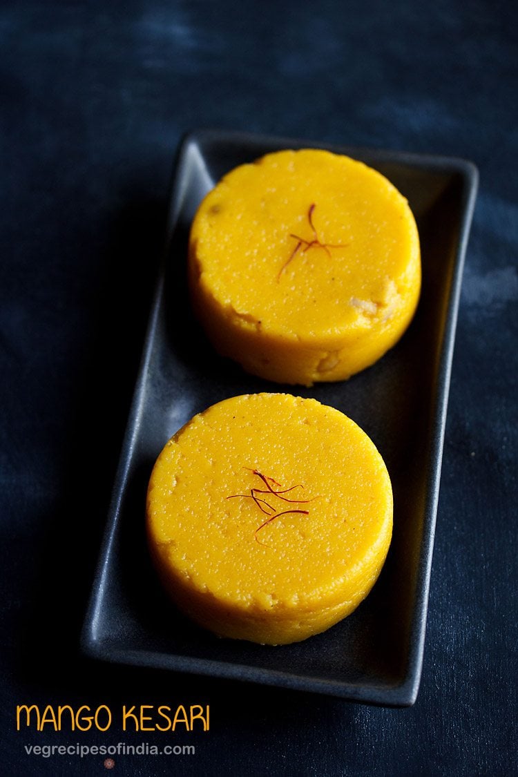 mango kesari garnished with saffron and served on a black platter.