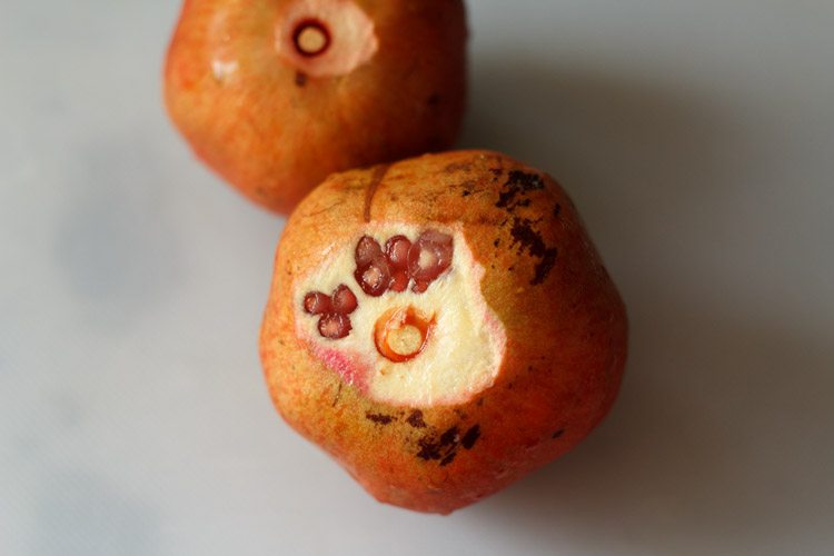 two whole pomegranates on a white table to make pomegranate juice recipe