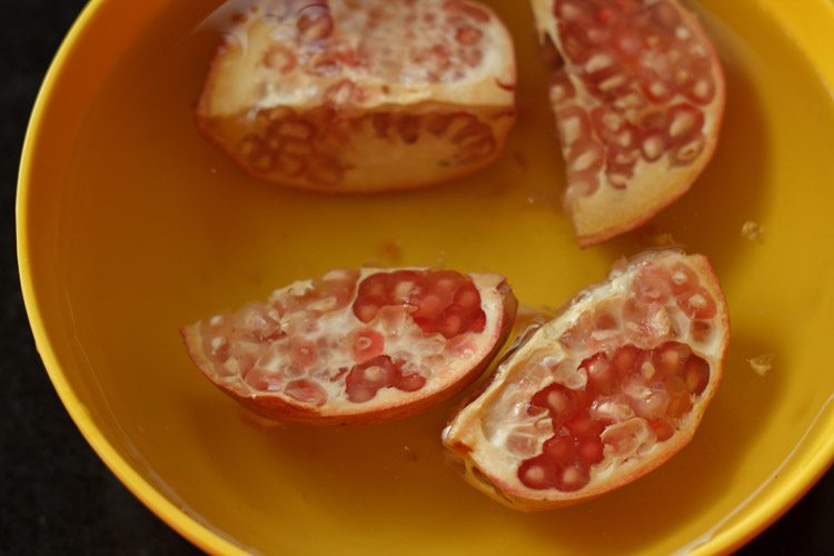 pomegranate quarters submerged in a yellow bowl of water