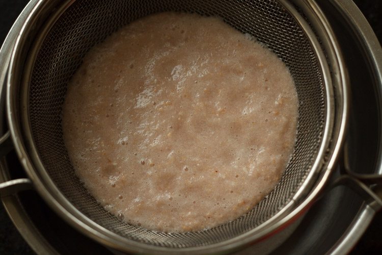 straining pomegranate juice through a mesh strainer