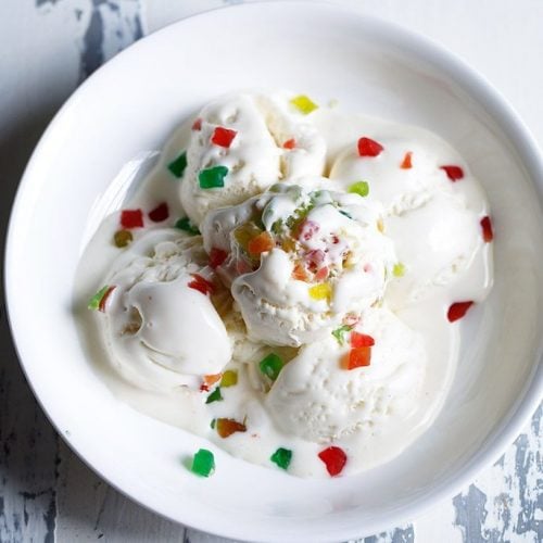 tutti frutti ice cream scoops garnished with tutti frutti and served in a white bowl.