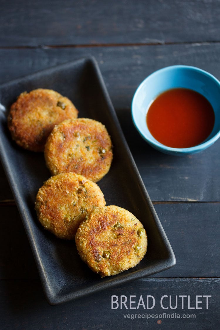 bread cutlet served on a black platter with a blue bowl of tomato ketchup kept on the right side and text layovers.