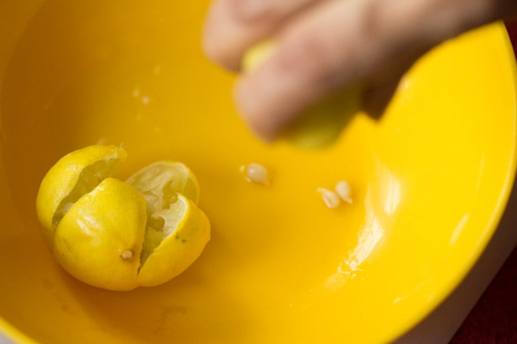 lemon being squeezed to get some juice in a yellow bowl