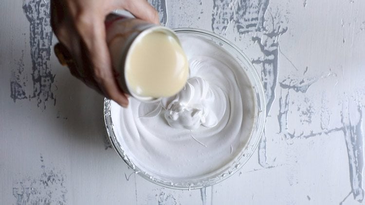 pouring in a can of sweetened condensed milk into the whipped cream