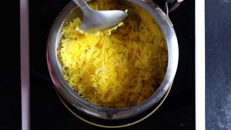 fluffing cooked zarda rice with a spoon.