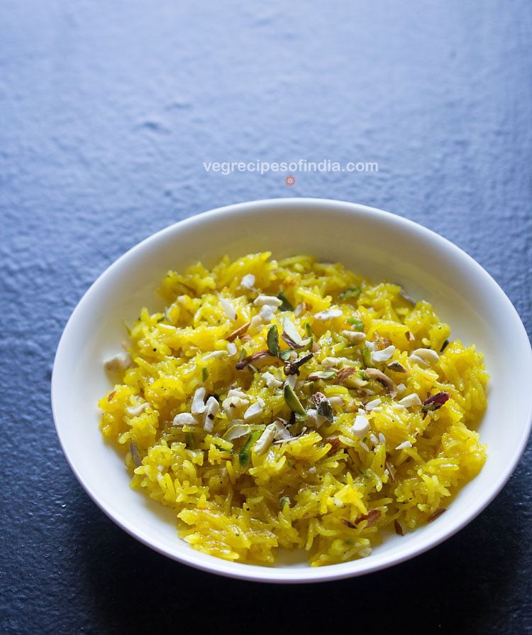 White shallow bowl filled with zarda pulao and topped with various chopped nuts.