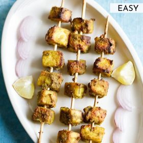 hariyali paneer tikka served on a white platter with onion slices and lemon wedges and text layovers.