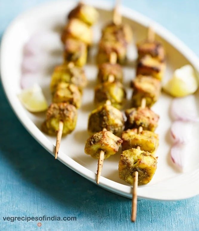 hariyali paneer tikka served on a white platter with onion slices and lemon wedges. 