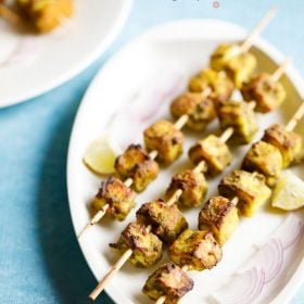 hariyali paneer tikka served on a white platter with onion slices and lemon wedges and text layovers.