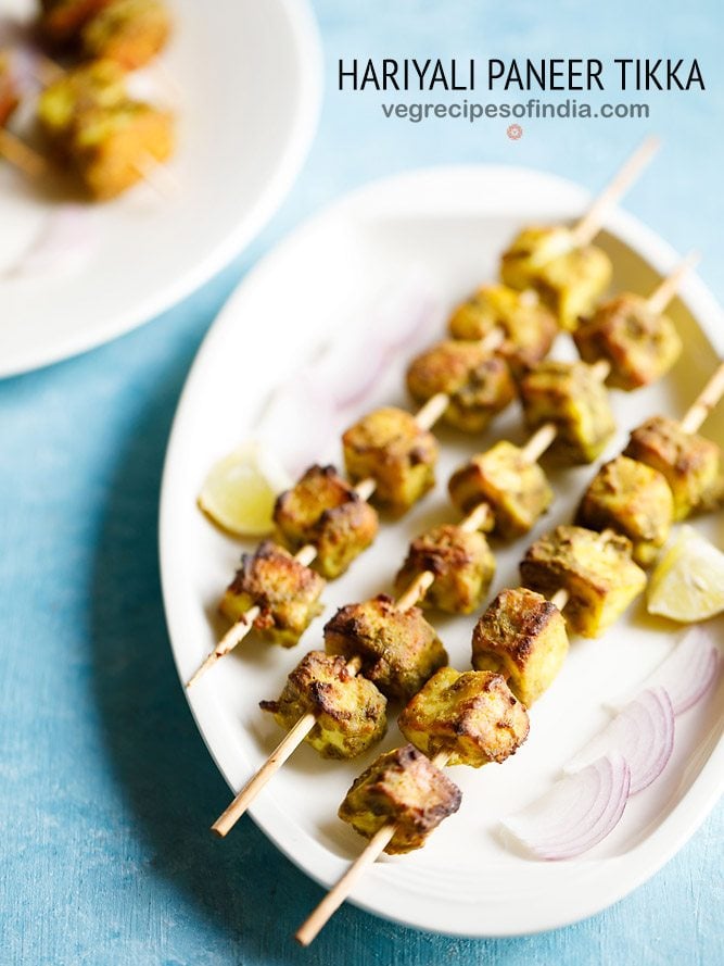 hariyali paneer tikka served on a white platter with onion slices and lemon wedges and text layovers.