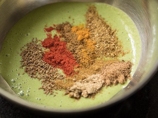 carom seeds and spice powders added to prepared green paste taken in a bowl. 