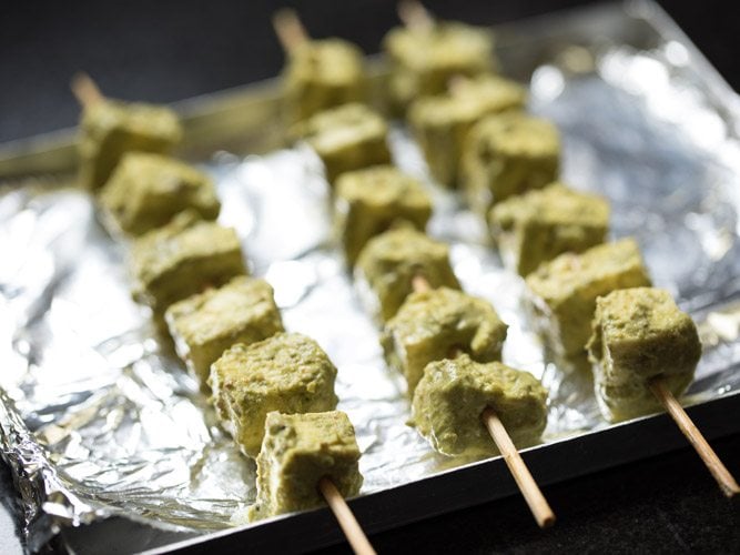 marinated paneer cubes threaded onto bamboo skewers and placed on a baking tray lined with aluminium foil. 