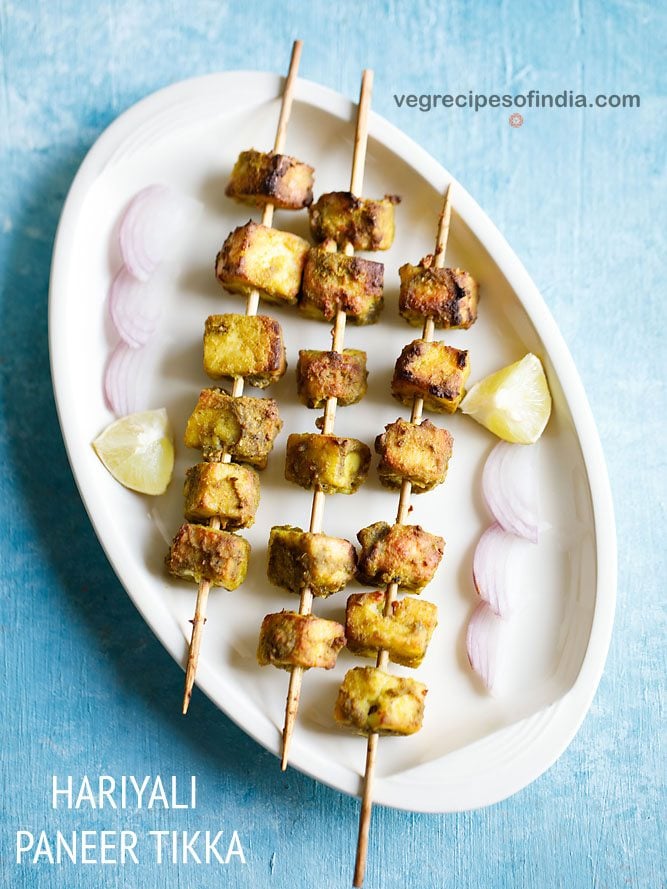 hariyali paneer tikka served on a white platter with onion slices and lemon wedges and text layovers. 