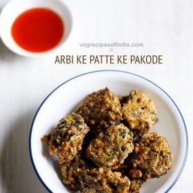 arbi ke patte ke pakode served in a blue rimmed white bowl with a small bowl of tomato sauce kept in the top left side and text layovers.