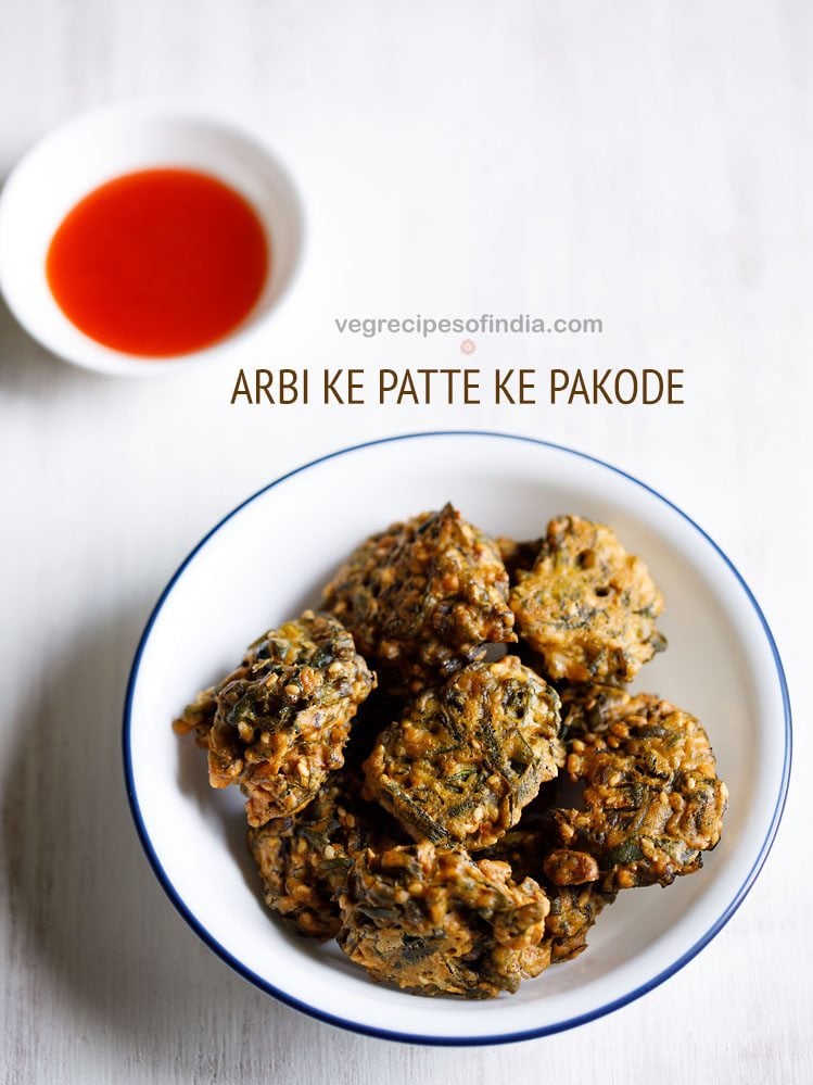 arbi ke patte ke pakode served in a blue rimmed white bowl with a small bowl of tomato sauce kept in the top left side and text layovers.