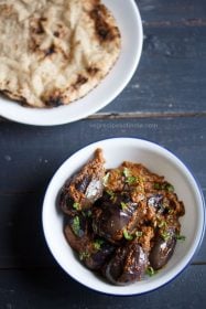 ennegayi garnished with coriander leaves and served in a white bowl with a plate of chapattis kept on the top left side.