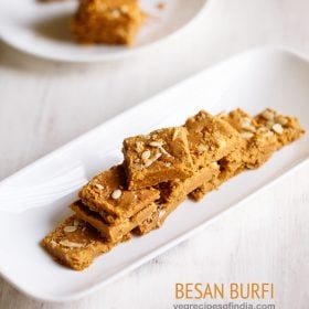 besan ki barfi pieces stacked on top of one another and served on a rectangular white platter with text layovers.