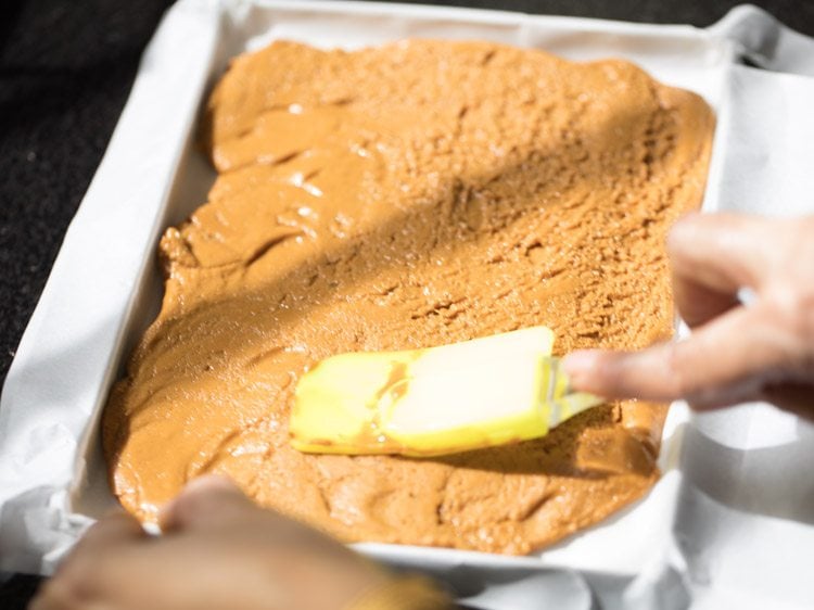 evening the barfi mixture layer with a spatula, in the tray. 