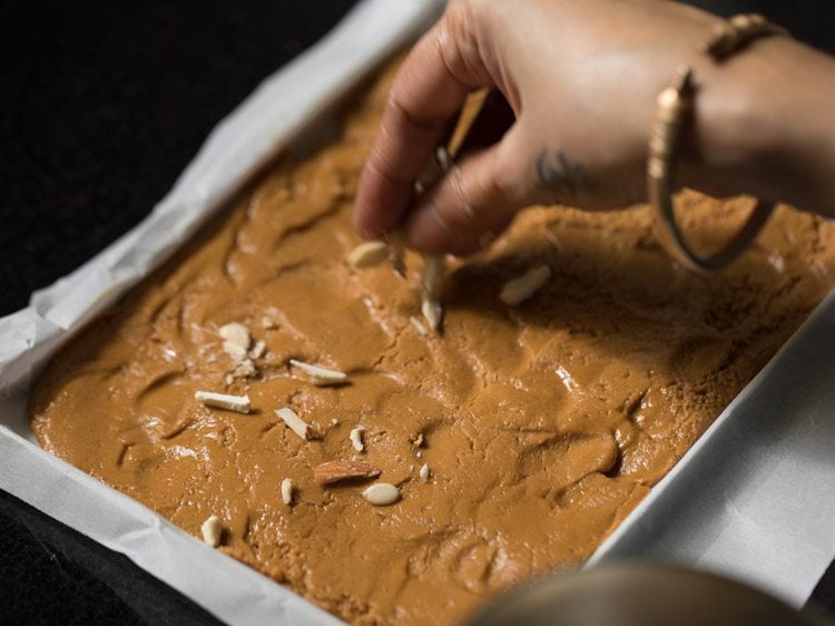 sprinkling chopped almonds, chopped cashews and melon seeds on top of the spread barfi mixture. 