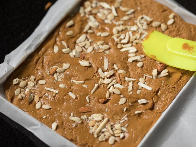 pressing the nuts and seeds with a spatula so that they stick on the barfi mixture. 