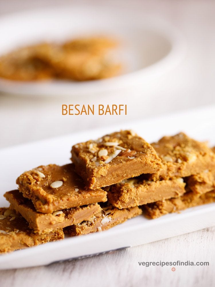 besan ki barfi pieces stacked on top of one another and served on a rectangular white platter with text layovers. 