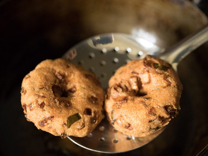 removing fried vada from hot oil with a slotted spoon. 